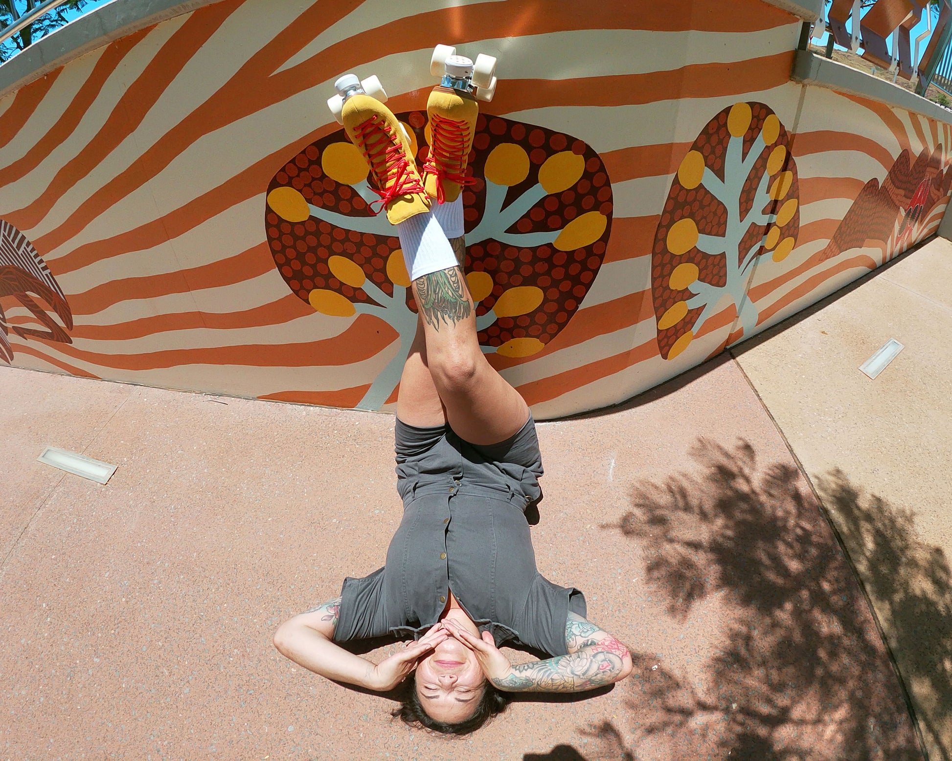 roller skater laying on her back with legs crossed wearing Chuffed Skates yellow roller skates with aboriginal painting wall behind