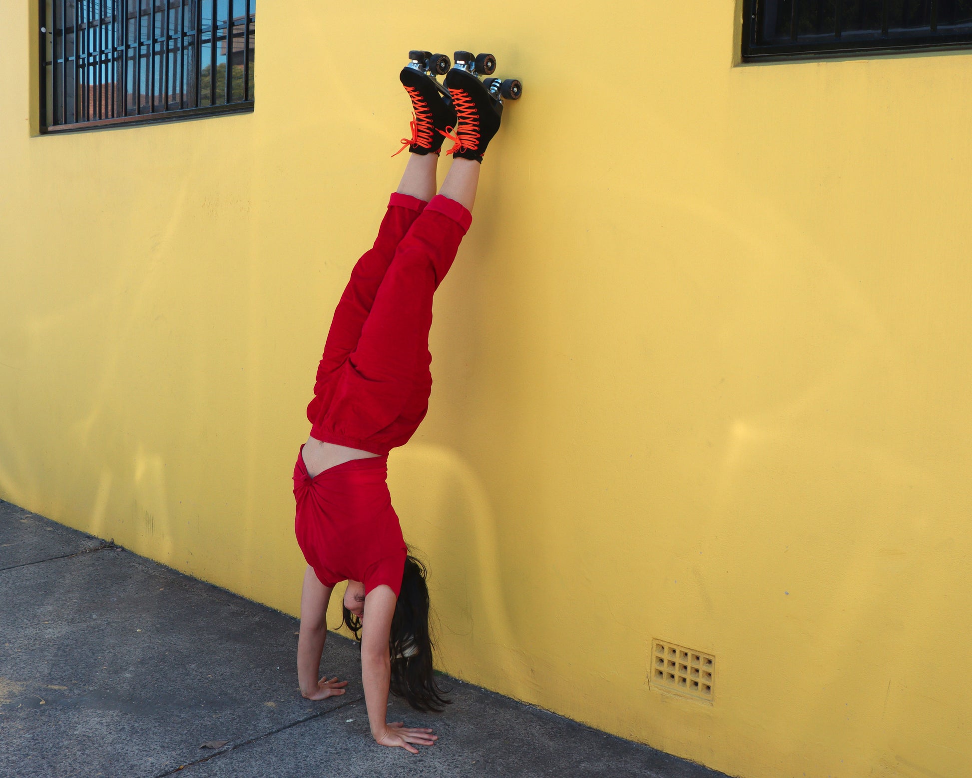 rollerskater doing a handstand wearing Chuffed Skates black roller skates on yellow wall